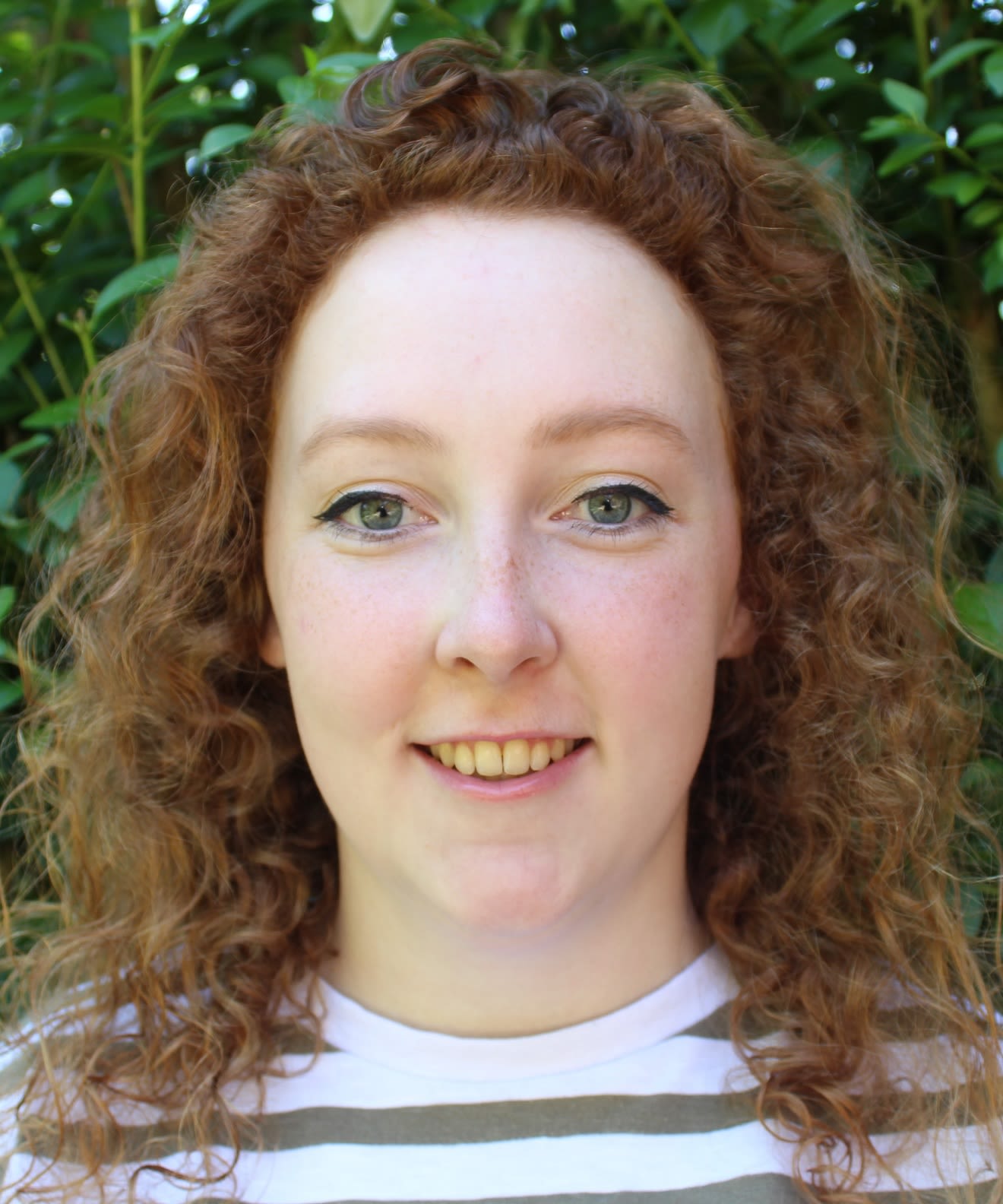 Close head and shoulders shot of woman with curly hair smiling at camera